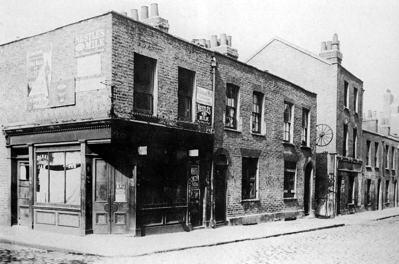 Berner Street and Dutfield's Yard as it was in 1909, 21 years after the murder of Elizabeth Stride. Dutfield's Yard is directly underneath and behind the suspended cart wheel. The International Workingmen's Club is immediately to the right of it (three storey building).